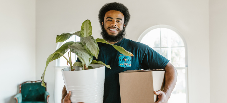A worker from long distance moving companies Colorado holding a plant in one hand and carton box in the other.