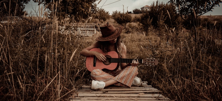 A woman sitting outdoors and playing a guitar.