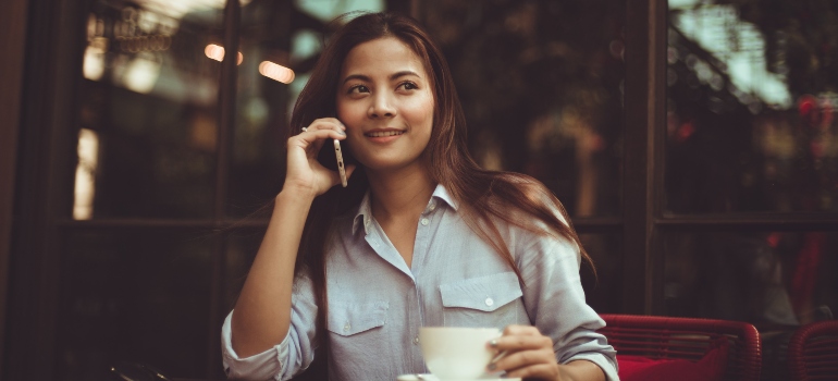 A woman talking on a phone while holding a cup of coffee.