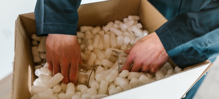 a mover outting glassess into a box full of packing peanuts 