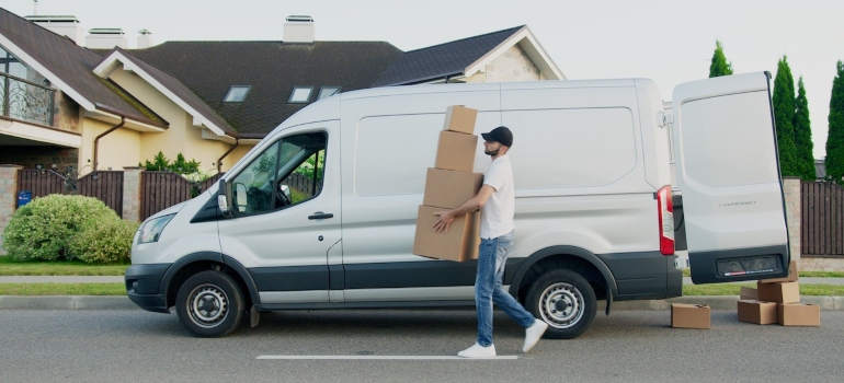 A man carrying boxes, standing next to a moving van