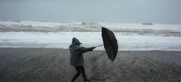 A person on the beach holding the umbrella, trying to save it from the wind.