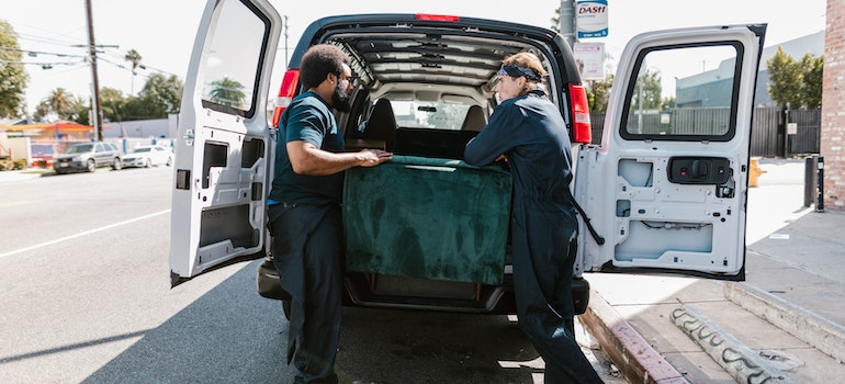 Two men putting a couch in a van.