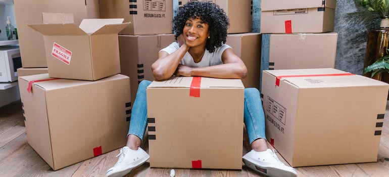 A woman smiling between carton boxes after leaving the packing process to long distance moving companies North Carolina.