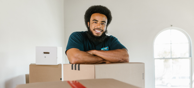 A man working for long distance moving companies North Carolina smiling over the carton box.