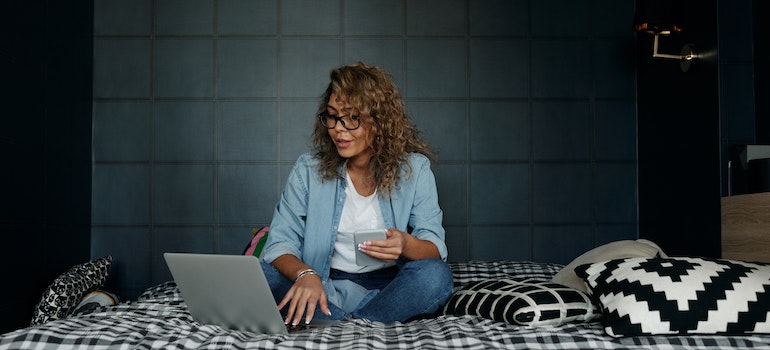 A woman looking at the laptop while sitting on a bed.