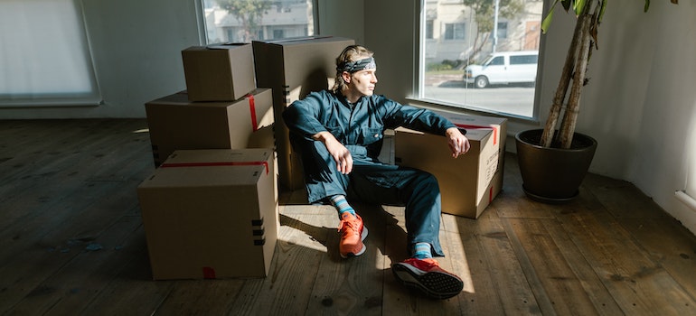 A man working for long dsitance moving companies Oregon sitting on a floor between boxes.