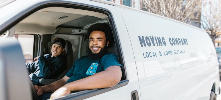Two moving company workers sitting in a van and getting ready to help someone with moving from Boston to Detroit.