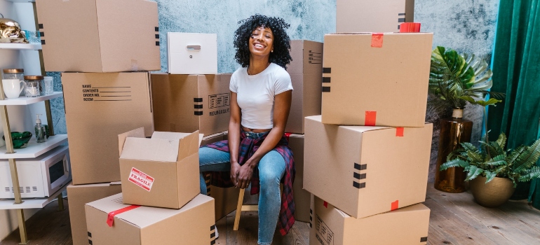 A woman smiling between boxes before moving from Florida to Maryland.