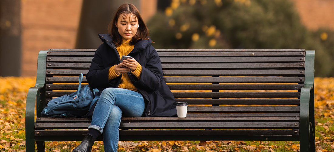A woman reading cross country moving companies Connecticut reviews on her phone while sitting on a park bench.