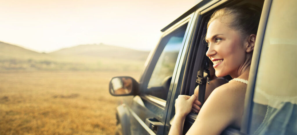 A woman looking through a car window and smiling.