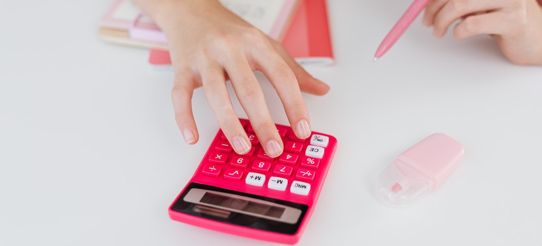A person calculating the cost of relocation with cross country moving companies New Mexicoon a pink calculator.