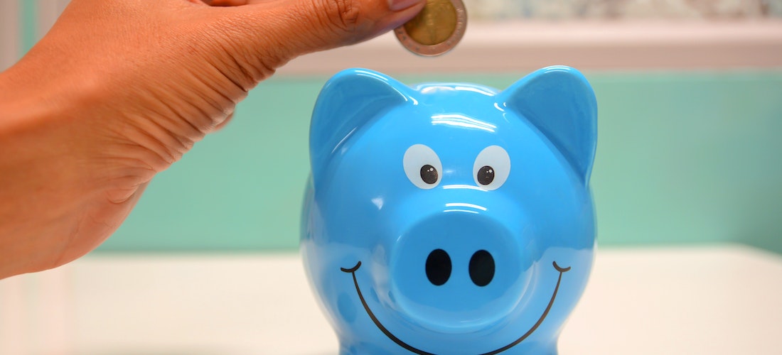 A person putting a coin in blue piggy bank