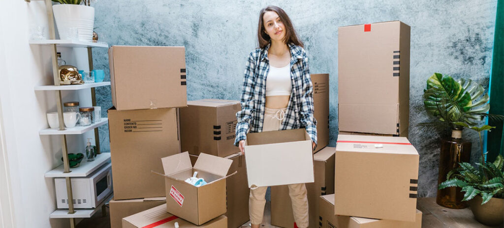A woman standing between many carton boxes, thinking about cross country movers Arizona has.