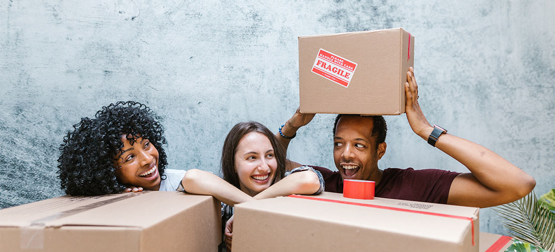 Three friends smiling behind moving boxes