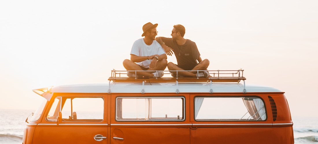 Two men sitting on the top of a van and talking