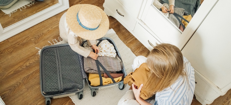 Two women who have enough reasons for relocation packing their suitcase.