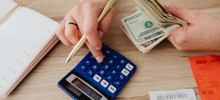 Person calculating on calculator, holding money