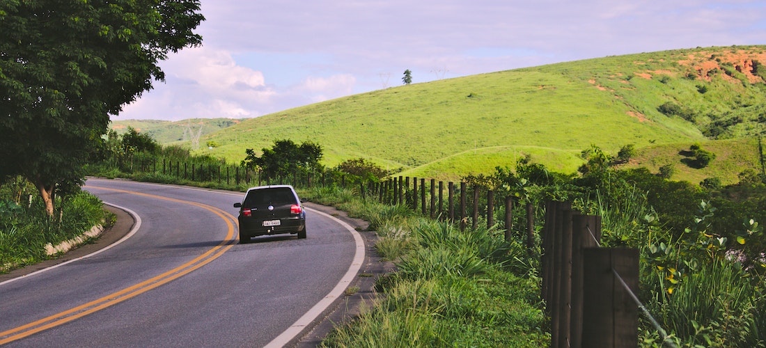 A car on the road next to a green hill