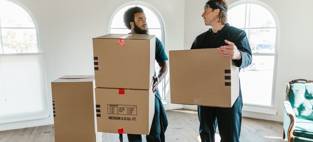 Two men from cross country moving companies South Carolina looking at each other while carrying boxes