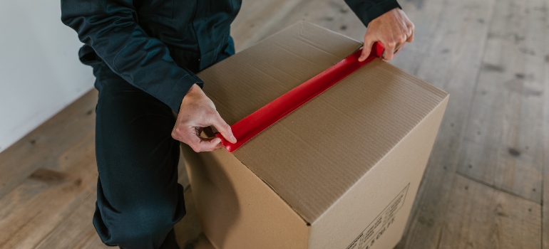 packer from long distance moving companies Castle Rock CO putting red tape on a cardboard box