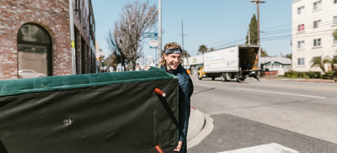 A man who is working for cross country moving companies New York holding a green sofa in the street
