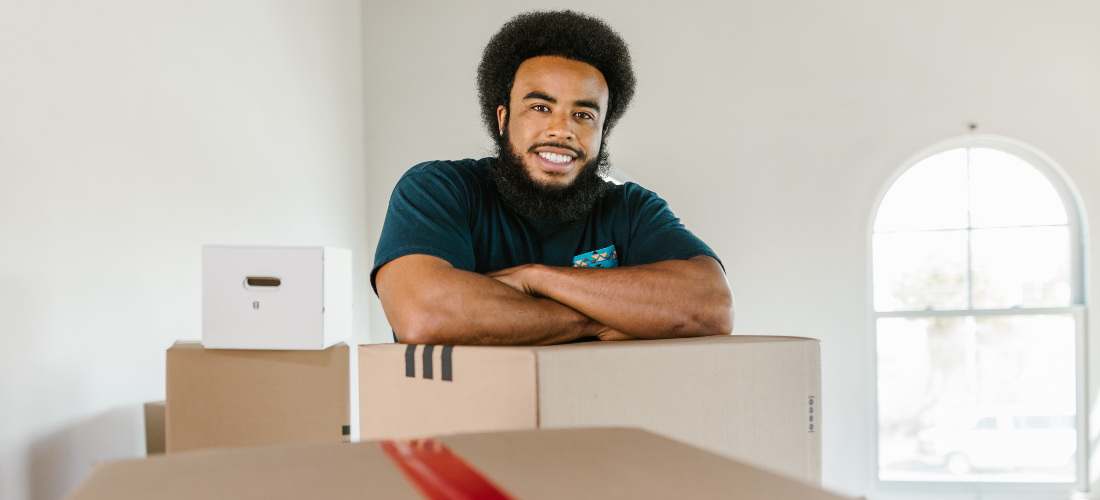 A man working for long distance moving companies North Carolina smiling over the carton box.