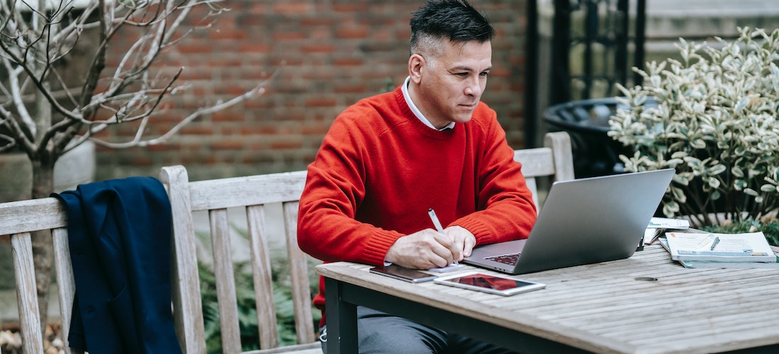 A man in a red sweater reading long distance moving companies Washington reviews on his laptop.