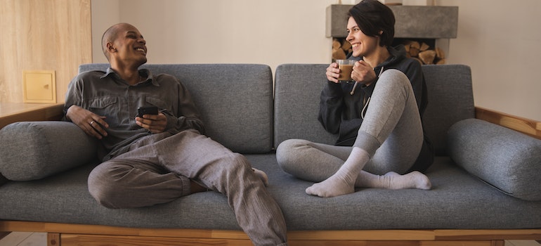A couple sitting on a couch, talking and drinking coffee