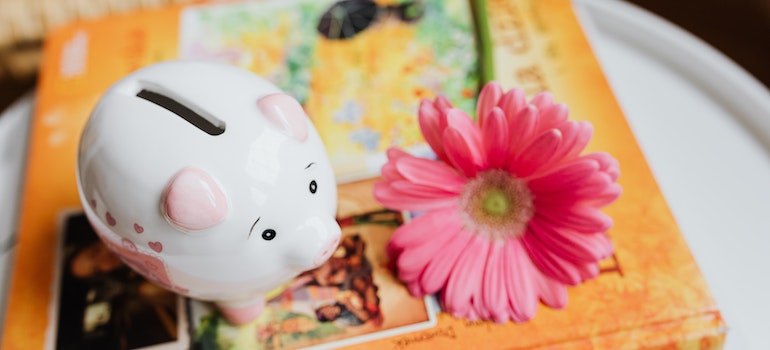 A piggy bank on a book, with a pink flower next to it.
