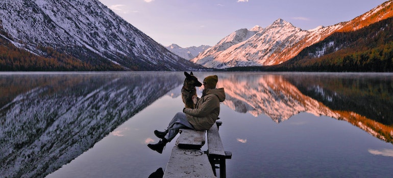 A woman sitting with a dog next to a lake.