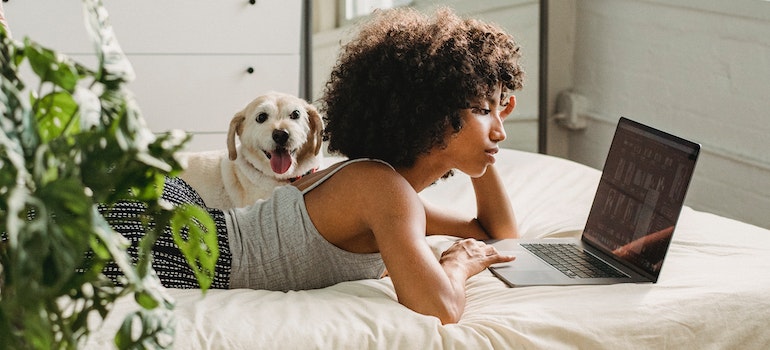 A woman laying on the bed and reading long distance pet relocation guidelines on her laptop.