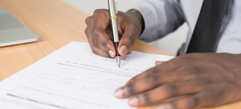 A person is holding a pen and signing a document, which is needed when moving to Switzerland from US.