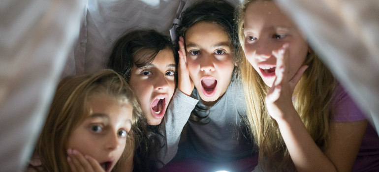 Four girls inside a tent with a flashlight.