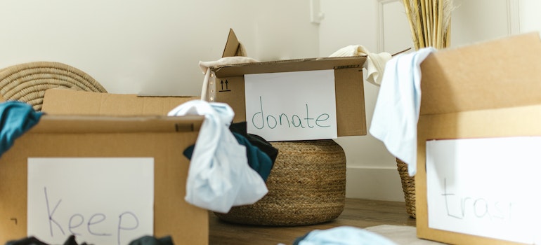 A lot of clothes and a box that says "donate" as a way of preparation for move on a low-income budget