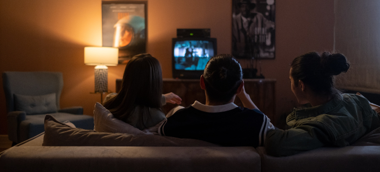 Three people are sitting on a couch and watching a movie.