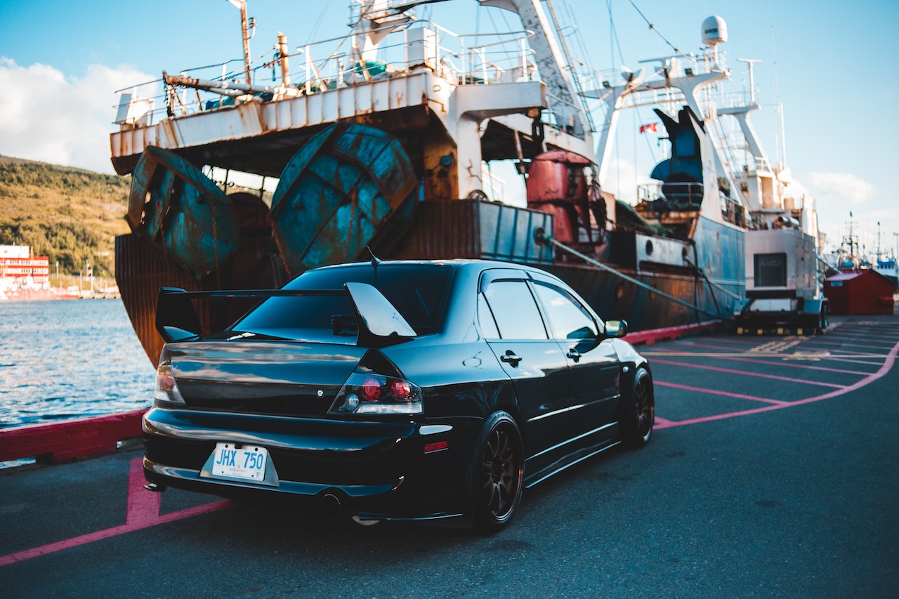 A car next to a ship ready to be loaded and transported