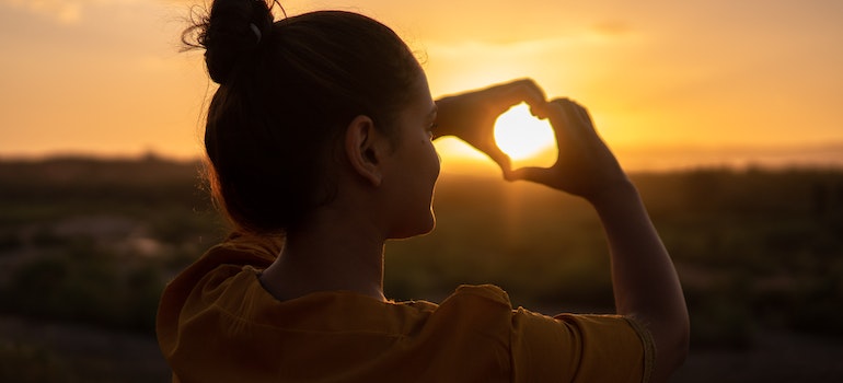 A woman making a hear sign with her hands during the sunset