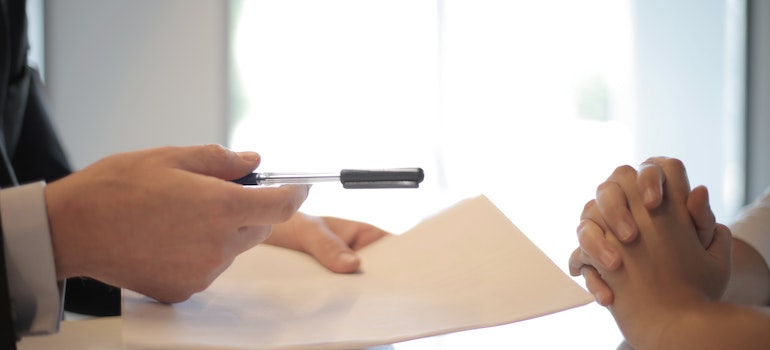person handing a pen to another person to sign a document about insurance and liability coverage