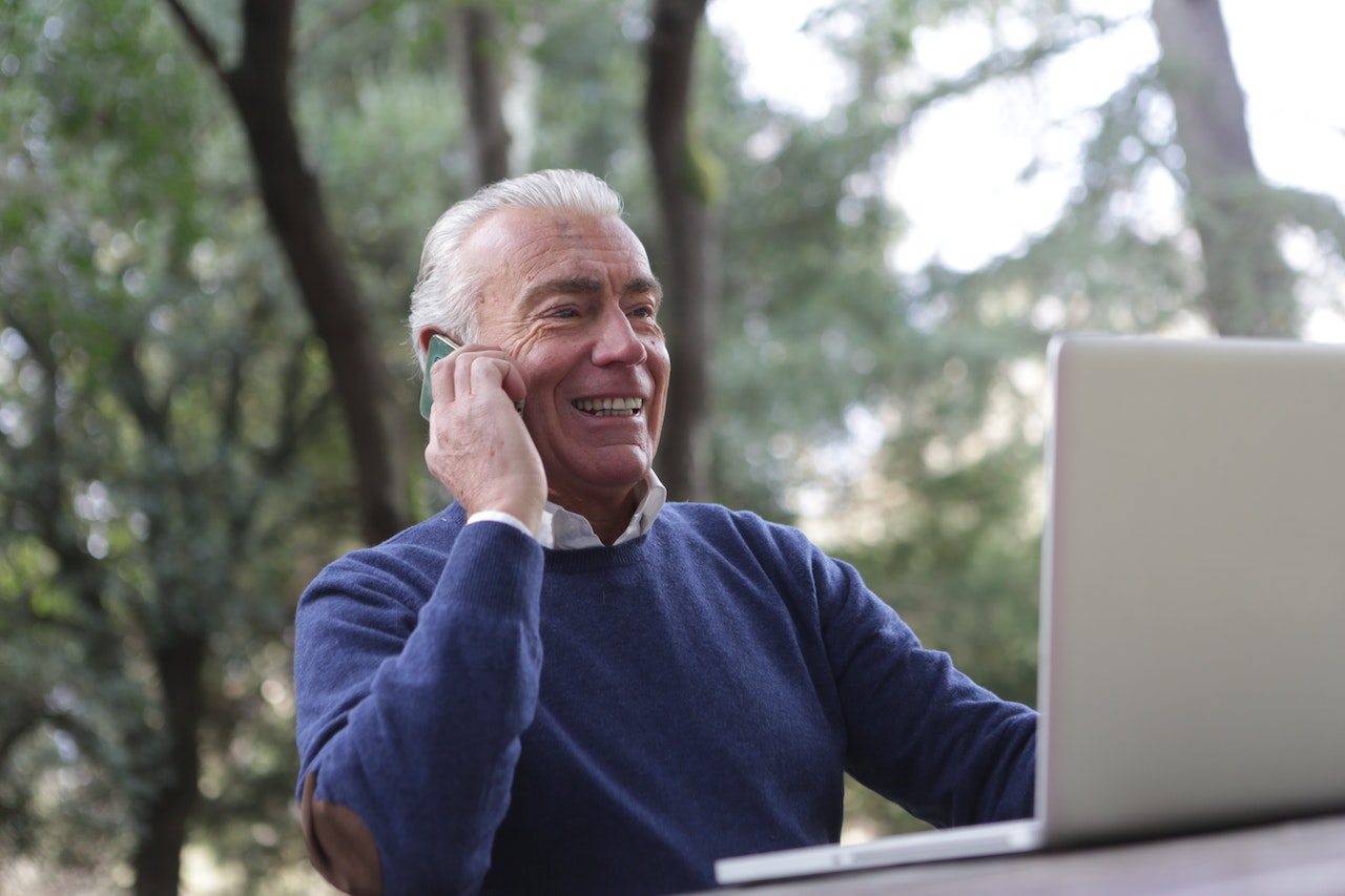 An elderly man speaking on the phone in front of his laptop