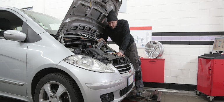 A car mechanic inspecting a silver car in a shop