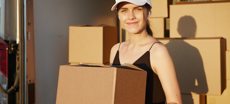 Woman with a cap, earpods and strap black top holding boxes during a move