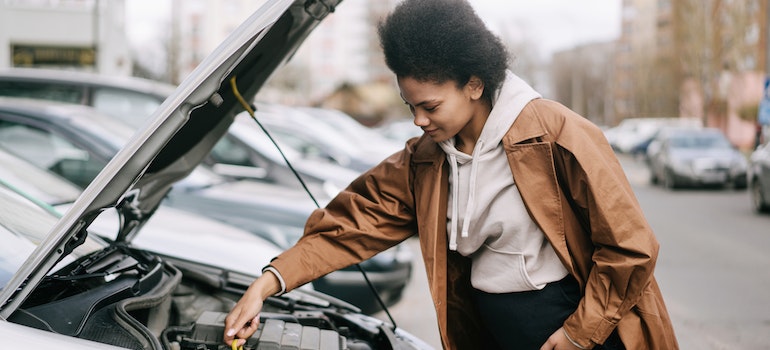 A woman in a brown coat checking for oil in her car