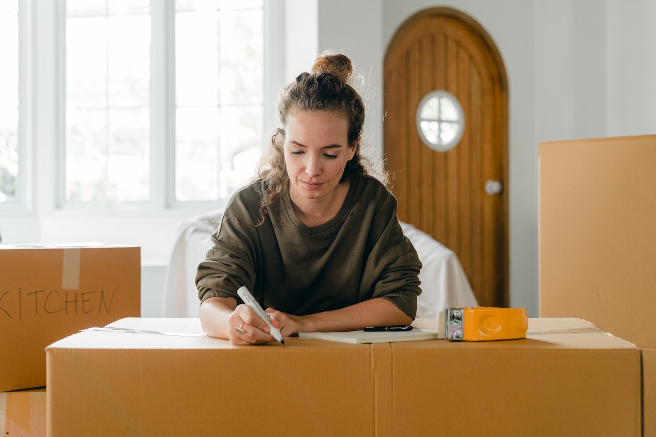 A woman writing on a cardboard box to create a moving timeline for post-moving tasks