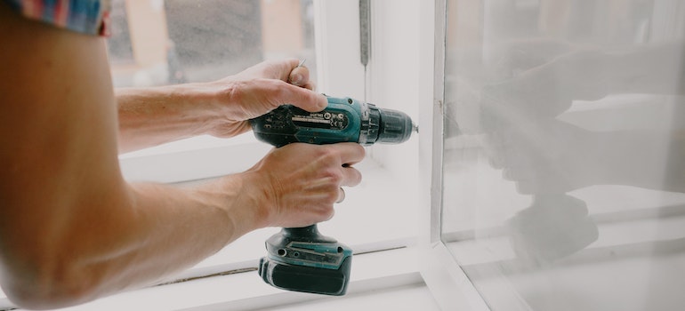 A perosn using a power drill as one of the tools for DIY home repairs after a move