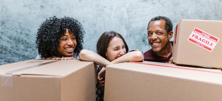 Three people standing behind cardboard boxes and laughing