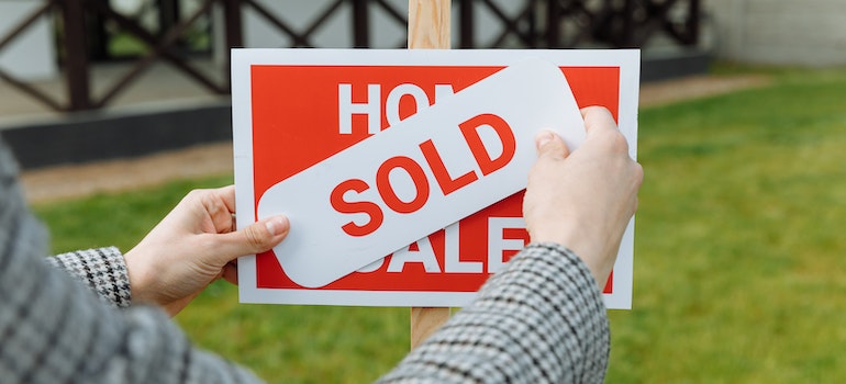 Woman putting a sold sticker on a sign saying home for sale
