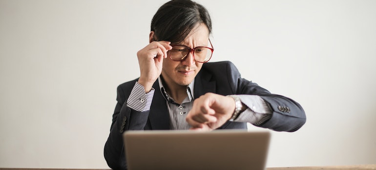 A man with red glasses looking at a watch trying to determine the best time to relocate in order to save money on a local move