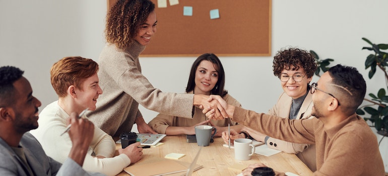 Two people shaking hands on a business meeting surrounded by other coworkers