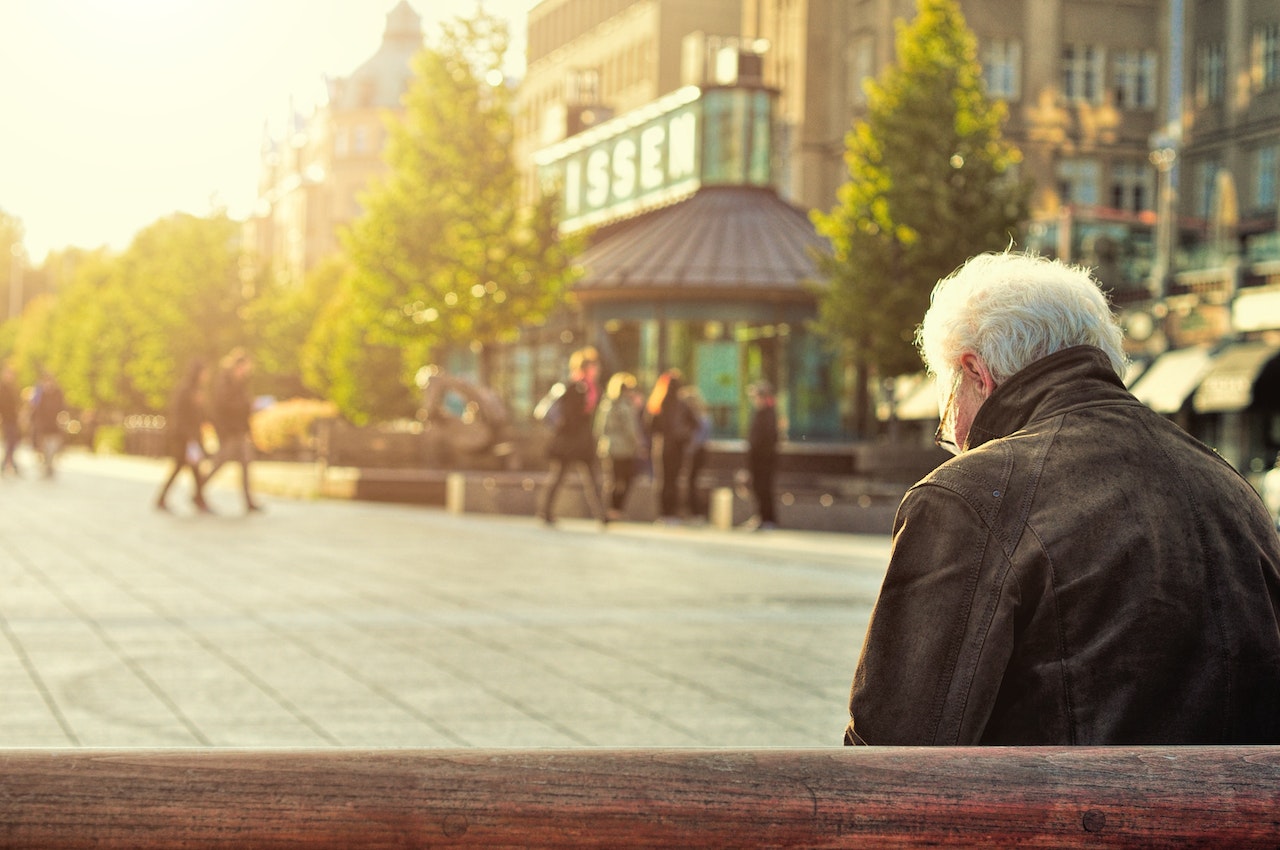 A retired man sitting on a bench in a city
